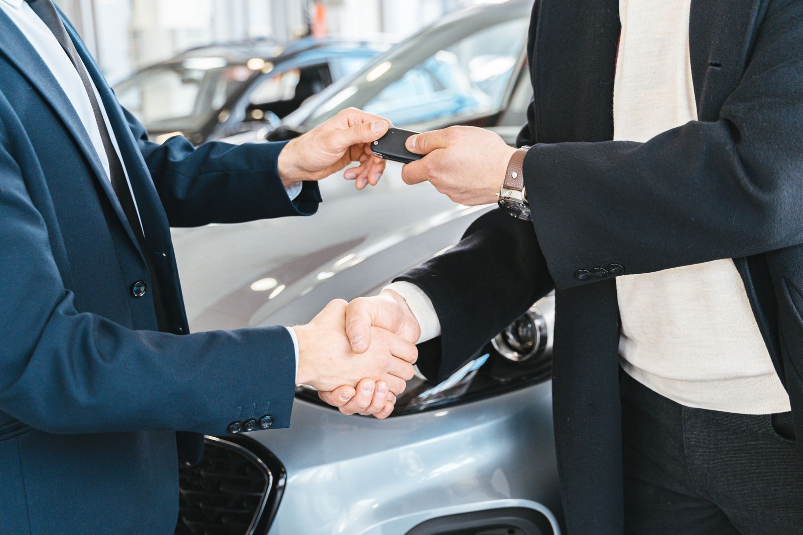 Two people exchanging car keys and shaking hands at a dealership